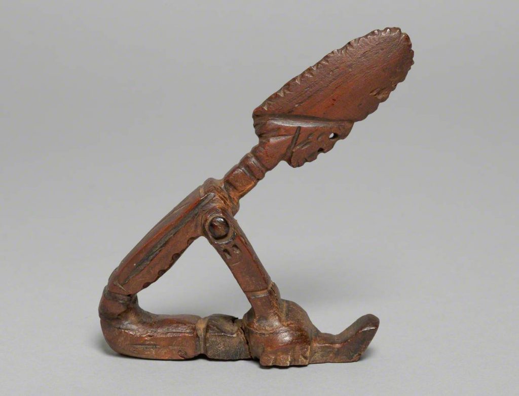 Brown woodcarving of a humanoid figure sat holding knees